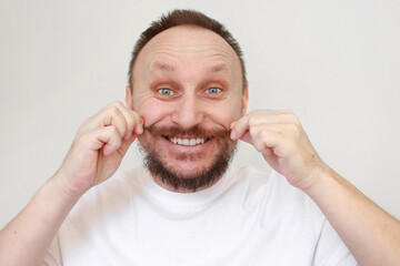 Portrait of happy caucasian bearded man touches his moustache in white casual t shirt smiles and looks at camera on white background. Lifestyle and positive emotions concept. Kind and happy face