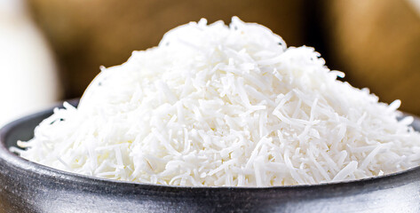 grated coconut, coconut shavings in a clay bowl, with ripe coconuts in the background, on a rustic wooden table , macro photography