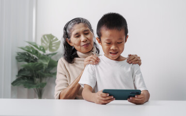 Playing mobile game together, Asian grandson and grandmother people sitting together at desk.