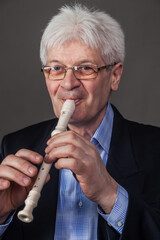 Portrait of an elderly musician in glasses and a dark suit playing a pipe. 