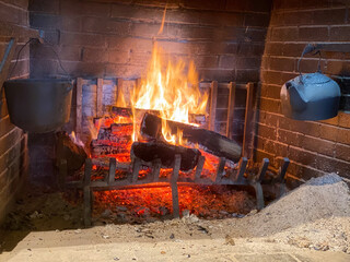 A roaring fire in a large fireplace with a cast iron kettle.