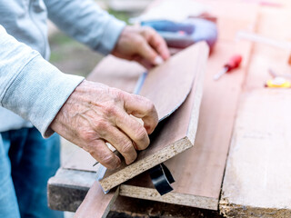 Close-up of an old man's hands fixing wooden planks. Selective focus.