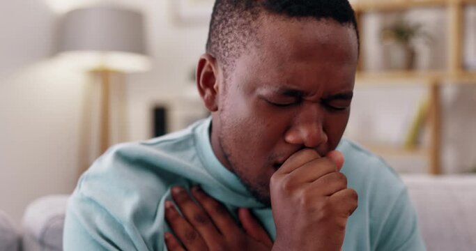 Sick, cough and man on a sofa in the living room in recovery from covid, flu or cold at his house. Healthcare, illness and African male with a chest infection, allergies or throat problem in his home