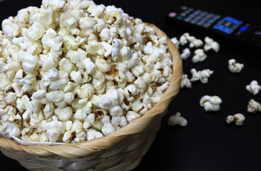 Popcorn in a wicker basket and a TV remote next to it - Patlamış Mısır