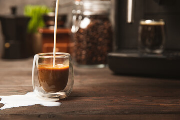 Black coffee in a glass and cream. Pour cream or milk into espresso. Coffee drink on black table background.Barista. Coffee house concept. Place for text.