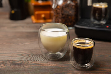 Black coffee in a glass and cream. Pour cream or milk into espresso. Coffee drink on black table...