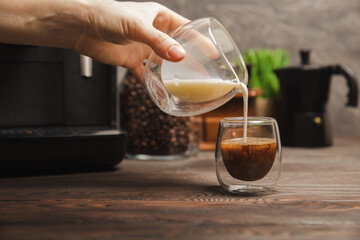 Black coffee in a glass and cream. Pour cream or milk into espresso. Coffee drink on black table background.Barista. Coffee house concept. Place for text.