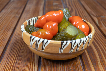 Mixed pickles of cucumbers and red bell peppers. Pickles in Romanian traditional clay bowl on wooden table.