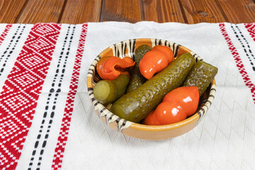 Mixed pickles of cucumbers and red bell peppers. Pickles in Romanian traditional clay bowl on...