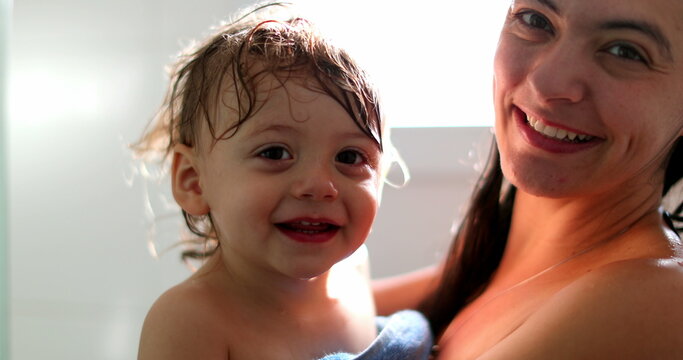 Mother holding baby after shower, cute toddler blinking to camera. infant waving hello or goodbye with hand