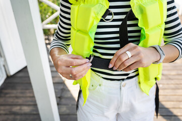 The girl is standing in a light green life jacket on the pier and is preparing for a boat trip.