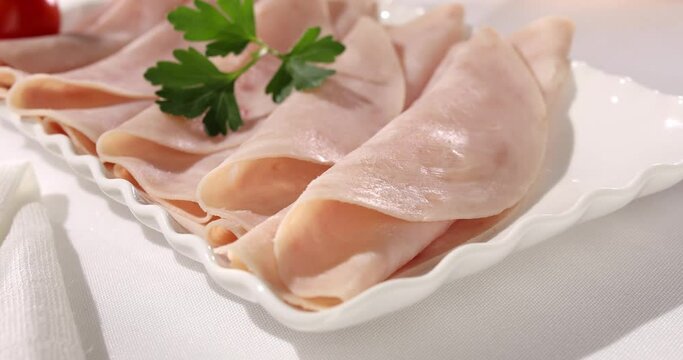 ham on a plate. meat delicacy with cherry tomato on a light background. turkey ham slices with parsley. cold appetizer on a white tablecloth. treat close-up.