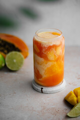 Tropical smoothie on a light background. Drink Lassi made of yogurt, papaya, mango, other tropical fruits, spices and ice. Close-up.