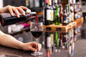 Close up of waiter pours red wine from bottle into glass at restaurant. Sommelier tasting wine in restaurant.