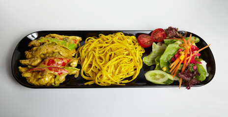 Grilled Chicken with Curry Sauce Linguine Pasta and Green Salad on Black Plate White Background