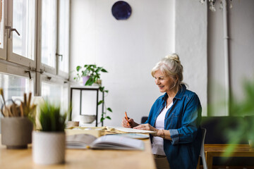 Smiling mature businesswoman writing in notebook while sitting at table in office