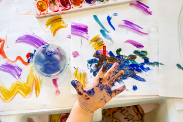 Toddler paints hand with colorful watercolor paint while painting on white paper