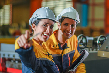 Man mentor and young employee trainee stand for operating machine looking see through camera monitor and point finger with happy fun cheerful mood. foreman couple engineer happy mood in factory
