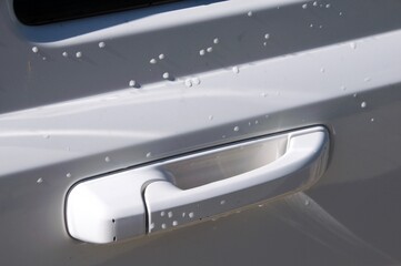 Close up white door handle on white car with rain drops and sunlight