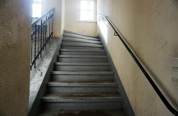 Verwittertes Treppenhaus von altem mehrstöckigem Haus mit beigen Wänden und grauer verwitterter Treppe mit schwarzem Eisengeländer vor Fenstern 