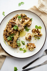 Baked cauliflower steak on white plate with cilantro leaves