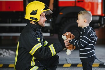 A firefighter take a little child boy to save him. Fire engine car on background. Fireman with kid in his arms. Protection concept.