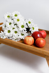 Red apples on a wooden tray with white flowers on a white background.