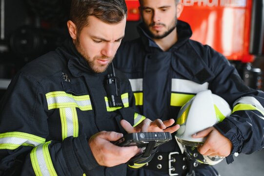 Portrait of two firefighters in fire fighting operation, fireman in protective clothing and helmet using tablet computer in action fighting