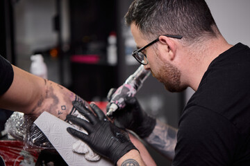 Close up tattoo machine. Tattooing. Man creating picture on his arm by a professional tattoo artist.