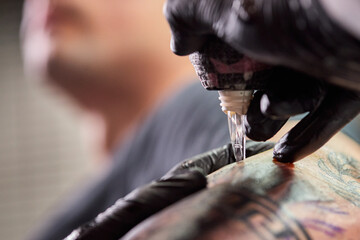 Close up tattoo machine. Tattooing. Man creating picture on his arm by a professional tattoo artist.