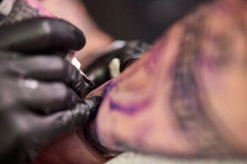 Close up tattoo machine. Tattooing. Man creating picture on his arm by a professional tattoo artist.