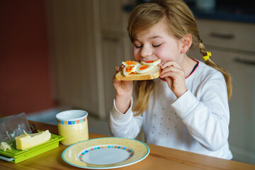 Little smiling girl have a breakfast at home. Preschool child eating sandwich with boiled eggs....