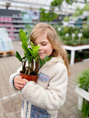 Cute girl holding potted plant in a flower shop. Little farmer choosing and buying green plants for...