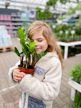 Cute Girl Holding Potted Plant In A Flower Shop. Little Farmer Choosing And Buying Green Plants For Home. Happy Child.