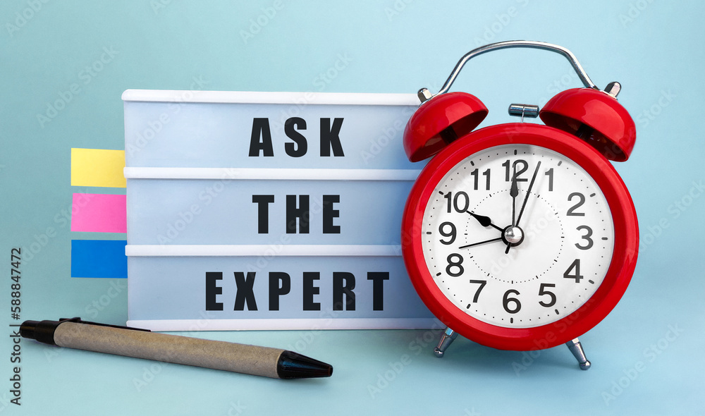 Poster text ask the expert written on the lightbox with alarm clock and colorfull stickers on blue backgrou