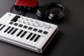 White midi keyboard, black headphones and read audio interface on a black background