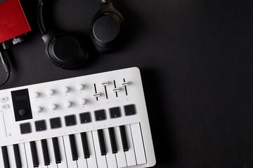 White midi keyboard, black headphones and read audio interface on a black background