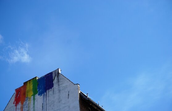 Wei&szlig;e hohe verwitterte Hausfassade mit bunten Farbklecksmalereien vor blauem Himmel bei Sonne am Mittag im Fr&uuml;hling