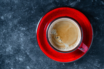 Red porcelain coffee cup with saucer over black background, top view, copy space, closeup. Hot...