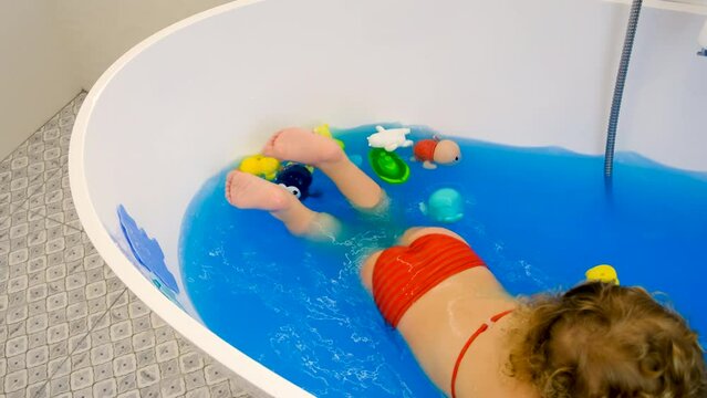 The child bathes in the bath paint blue color. Selective focus.