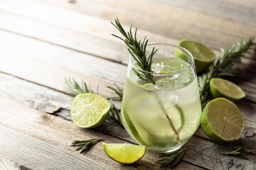 Gin tonic with ice, rosemary, and lime slices on an old wooden table.