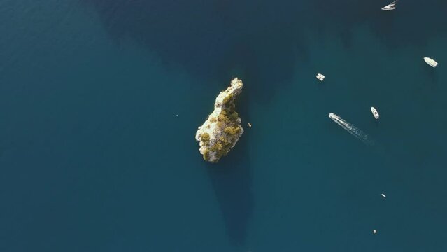 Aerial view of isolated rock in the middle of the sea on the coast of Palinuro with small boats sailing around, Salerno, Campania, Italy.
