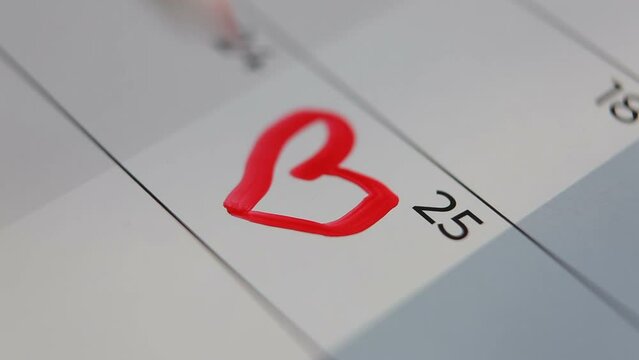 A man or woman draws a heart with a red marker on the calendar on the 25th.