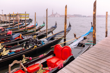 Fototapeta na wymiar Gondolas moored by Saint Mark square with Church of San Giorgio Maggiore in the background on foggy morning, Venice, Italia