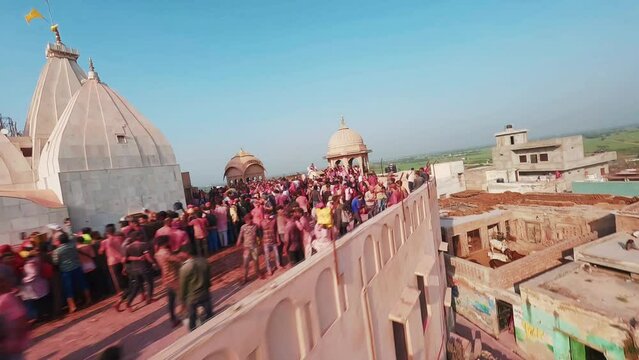 Aerial FPV view of people celebrating the Holi Colour festival at Shri And Baba Temple in Nandgaon, Uttar Pradesh, India.