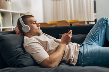 Fototapeta premium Side view of a Caucasian man resting on the sofa with his smartphone