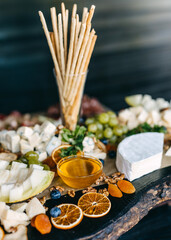 Buffet table with different cheese, honey, grapes and bread sticks at a party.