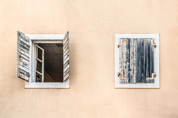 Closed and open window on a beige wall, close-up. Two antique windows with wooden shutters on a building in the Old Town of Budva, Montenegro. Element of old architecture in Stari Grad