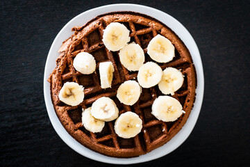 chocolate waffle with banana on a white plate with black background