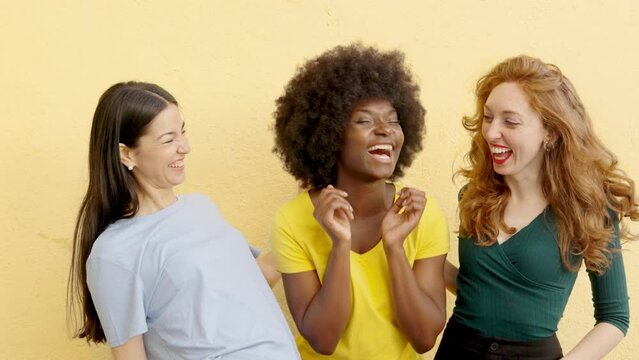 Three multicultural women laughing at camera outdoors